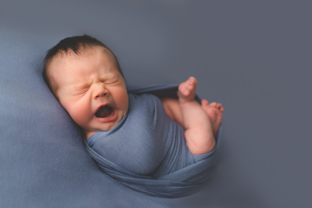 newborn baby wrapped in blue yawning
