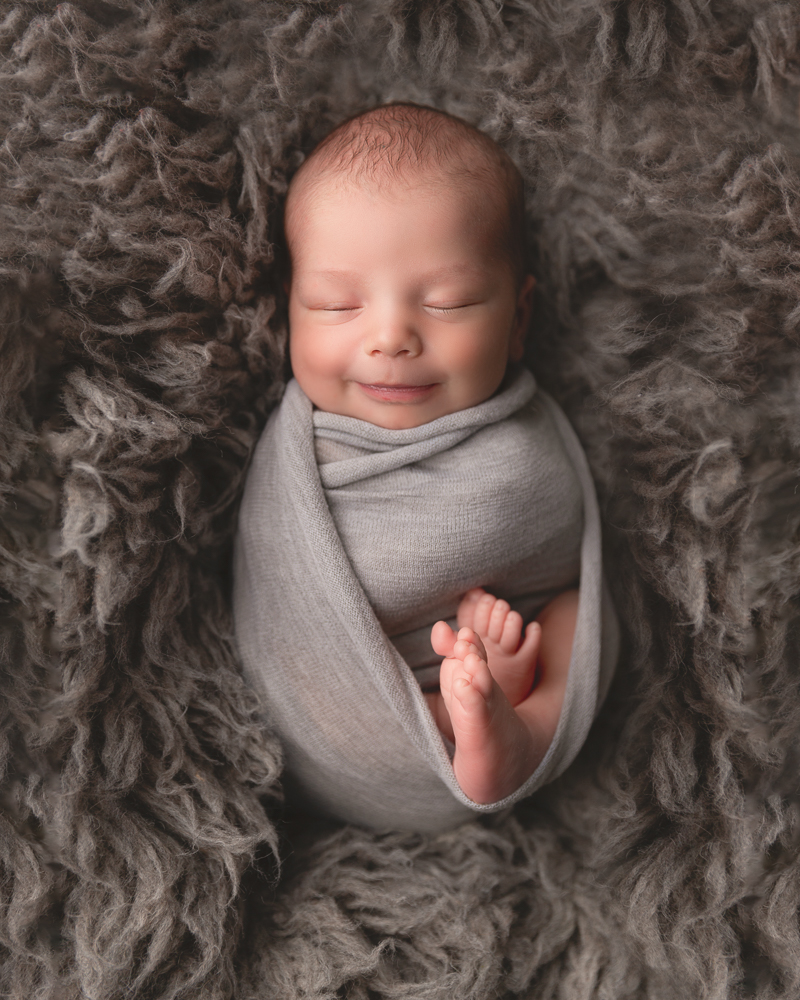 newborn baby boy wrapped in gray fabric