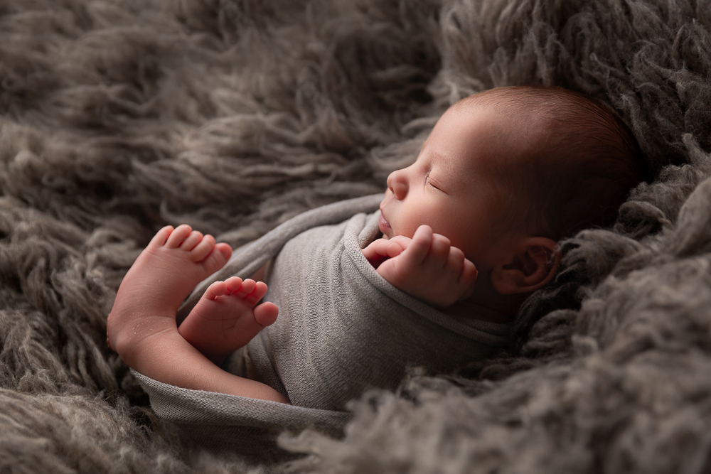 newborn baby boy wrapped in gray fabric