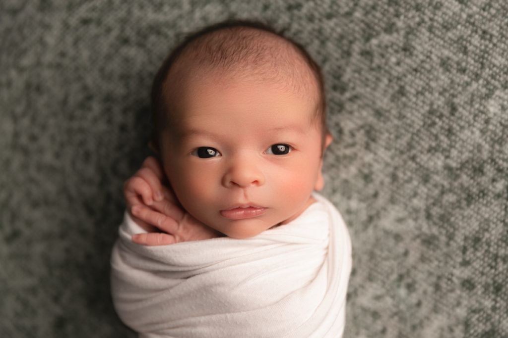 newborn baby swaddled in white, with eyes wide open